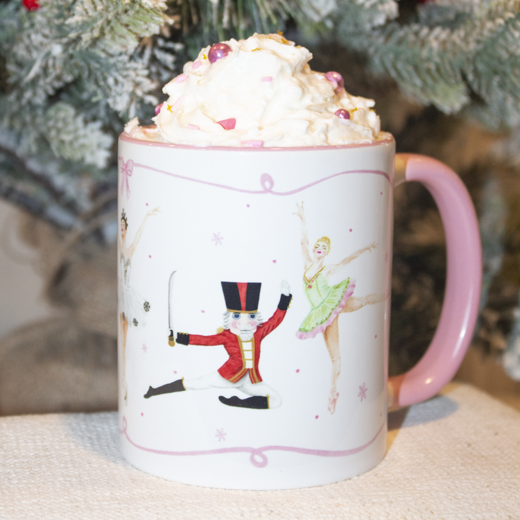 Nutcracker themed mug with multiple nutcracker characters shown. Pink handle and rim. Christmas tree in the background