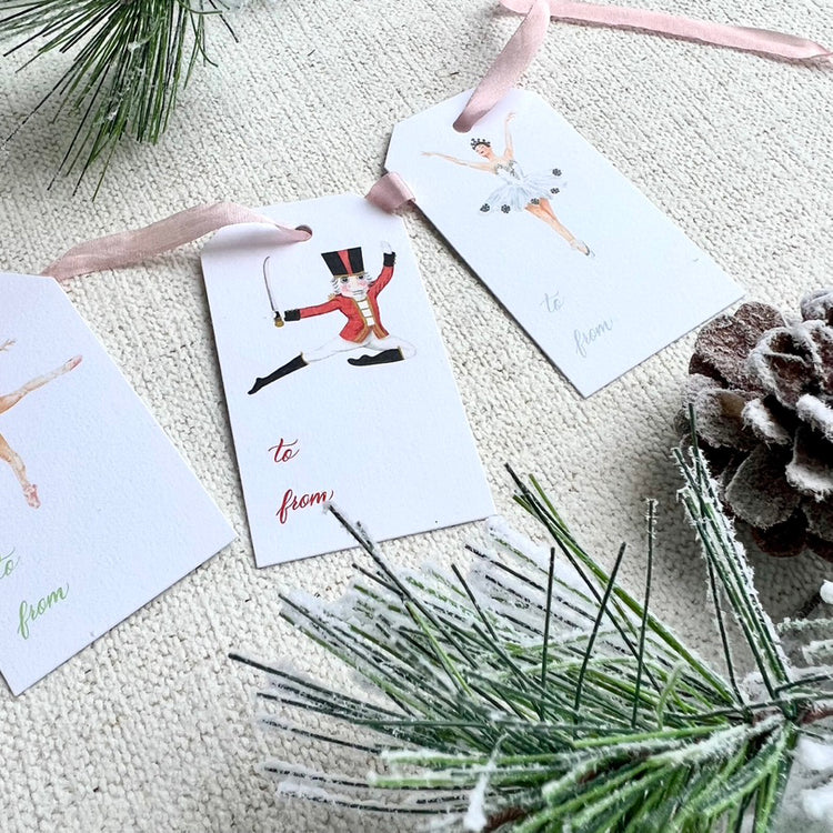 Nutcracker themed gift tags with a pink ribbon and faux greenery and a pinecone