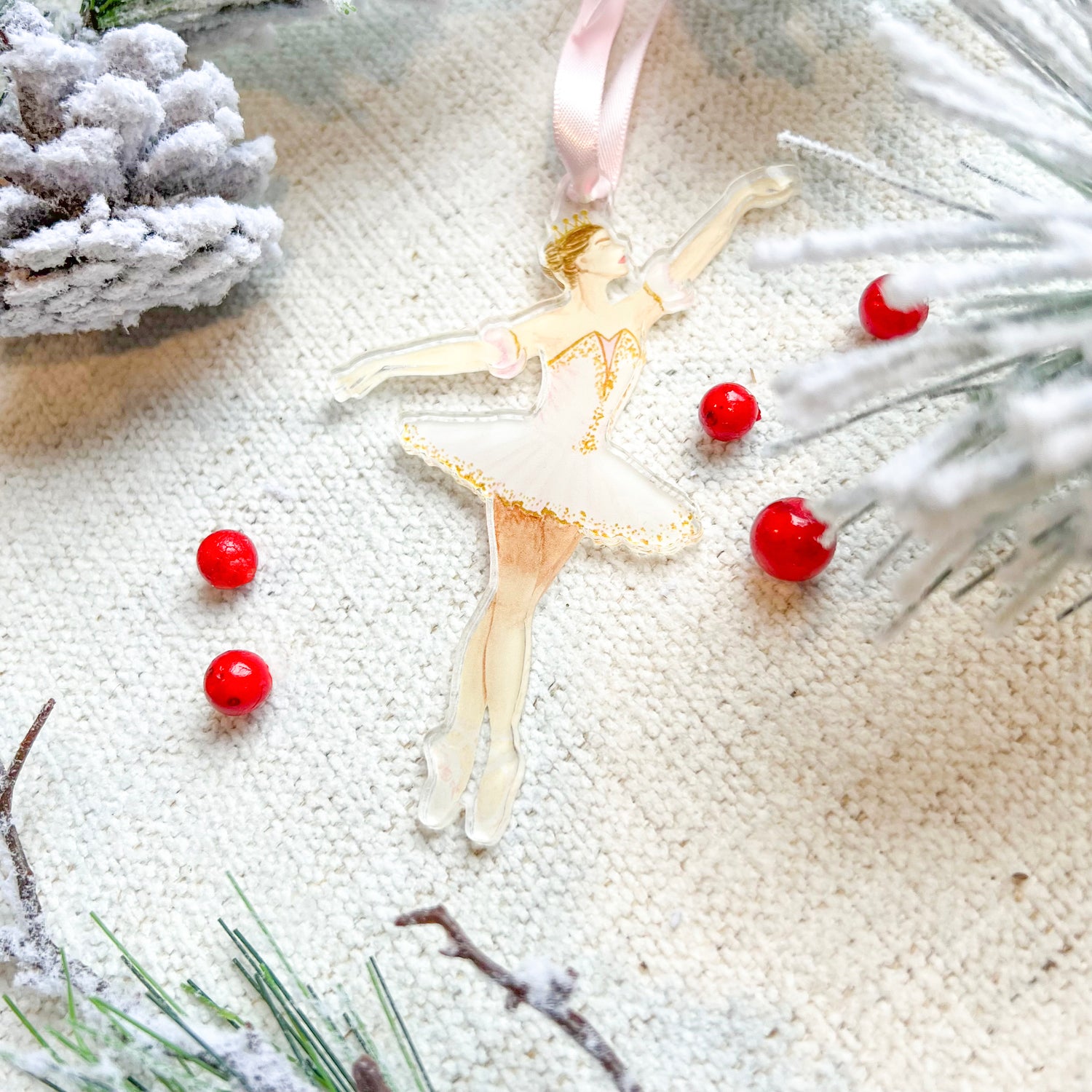 An ornament featuring the Sugarplum Fairy ballerina in her pink tutu. The background has berries and faux branches and a pinecone.