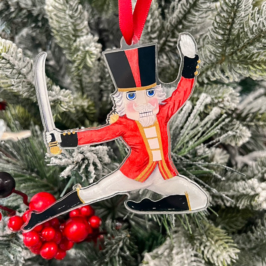 Nutcracker Prince ornament hanging on a tree  with a red ribbon.